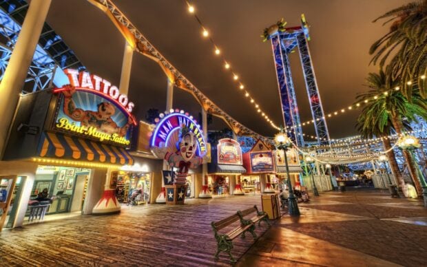 A vibrant amusement park walk lined with lit shops and colorful attractions under string lights at night