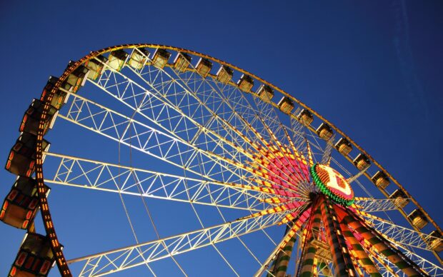 Large amusement park ferris wheel with colorful lights against clear blue sky