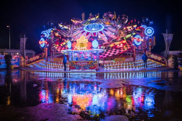 Neon lights reflecting on wet ground at an amusement park ride at night