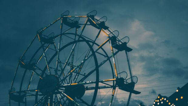 A Ferris wheel at the amusement park lit up against a cloudy evening sky