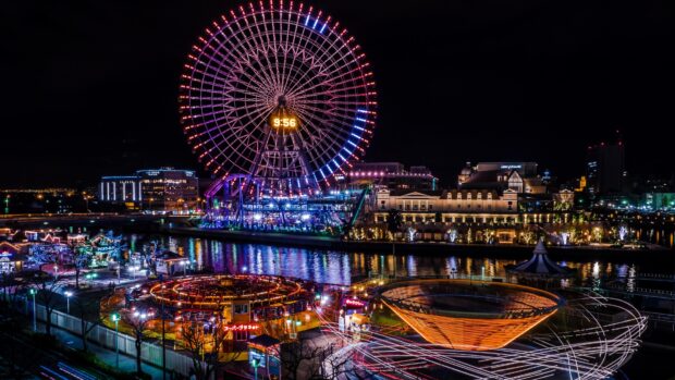 A colorful amusement park with a large ferris wheel and bright lights at night