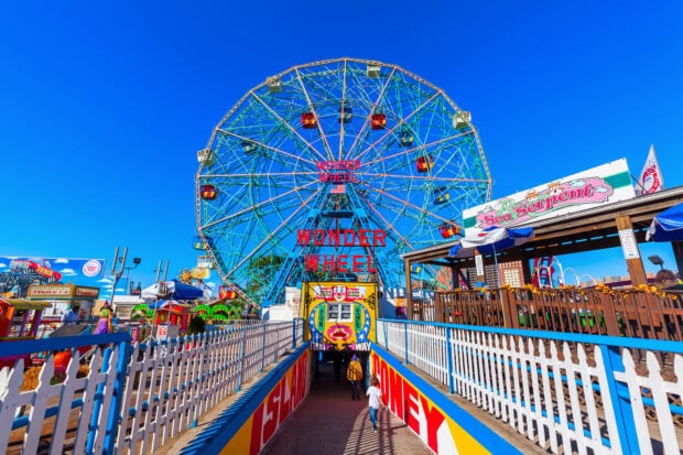 The amusement park with a large colorful ferris wheel and entrance pathway under clear blue sky