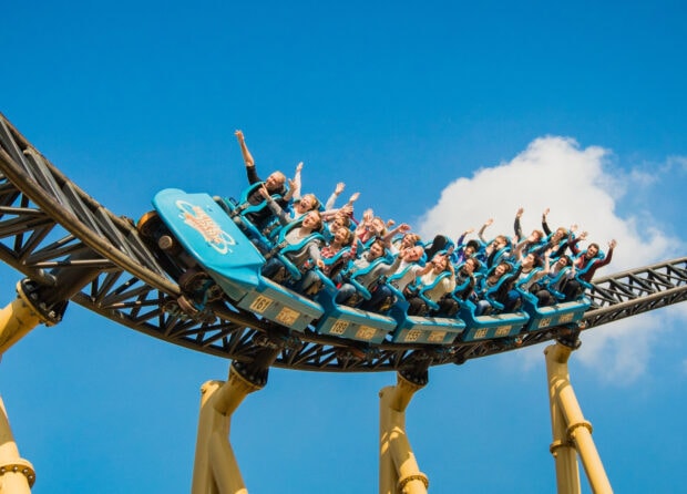 Thrilled riders enjoying the amusement park roller coaster ride under a clear blue sky
