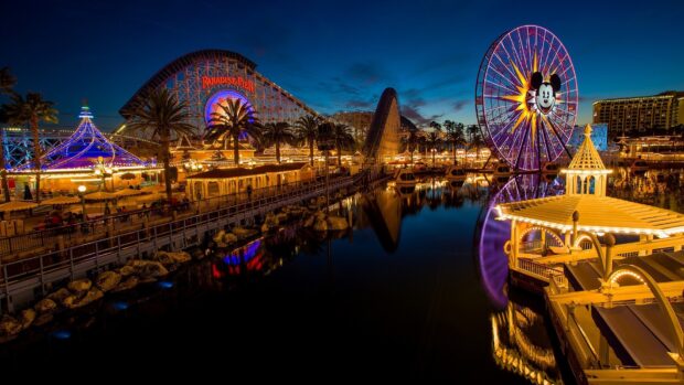 Vibrant amusement park at night with roller coaster and ferris wheel reflections in water