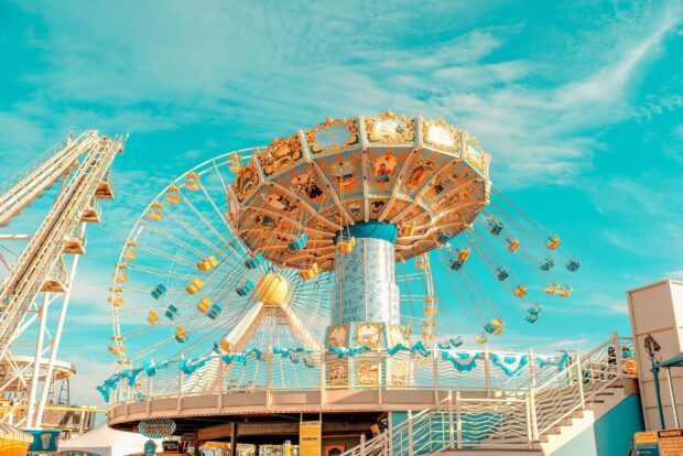 Vintage swing ride at amusement park under clear blue sky with ferris wheel in background