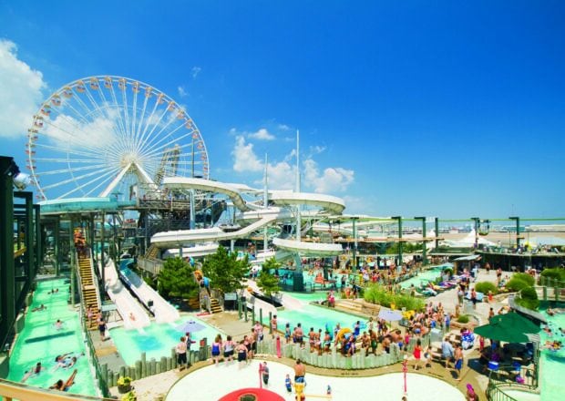 A crowded amusement park with waterslides and a large ferris wheel under a bright blue sky