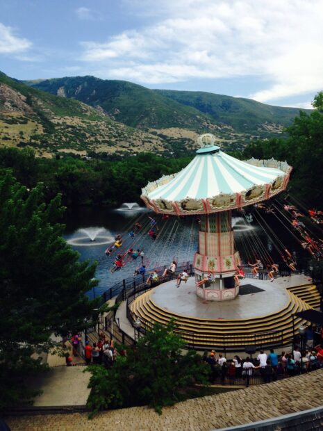 A swing ride at an amusement park surrounded by hills and water fountains