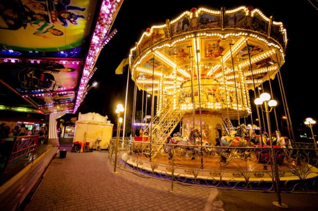 A brightly lit carousel at an amusement park with colorful horses and decorative lights at night