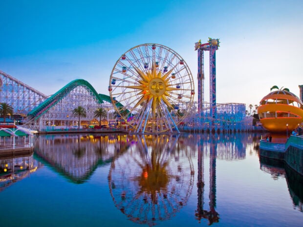 A vibrant amusement park with a large ferris wheel and roller coaster reflecting on calm water