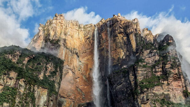 Angel Falls surrounded by rocky cliffs and green vegetation under a blue sky