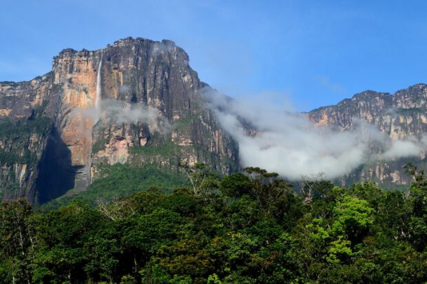 Angel Falls flowing down the mountain surrounded by lush green forest and blue sky