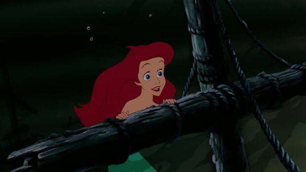 Ariel The Little Mermaid character looking excited near wooden shipwreck beams underwater