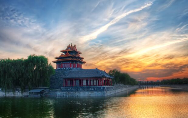 Ancient Asian architecture by river during sunset with dramatic sky and lush trees