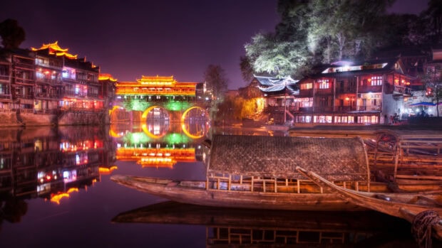 Traditional Asian river town with illuminated buildings and a wooden boat at night