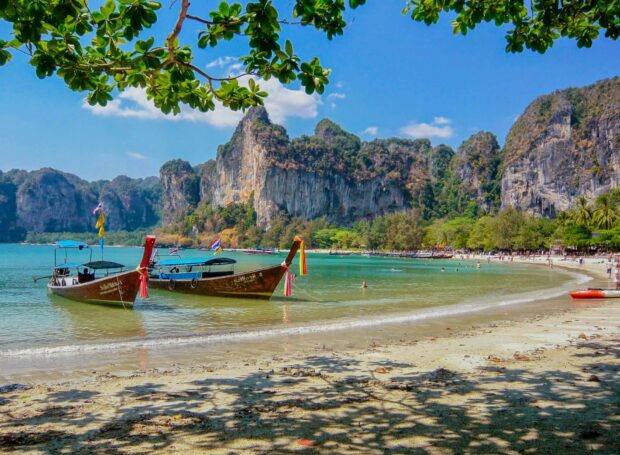 Traditional Asia boats anchored near a tropical beach with limestone cliffs and blue sky