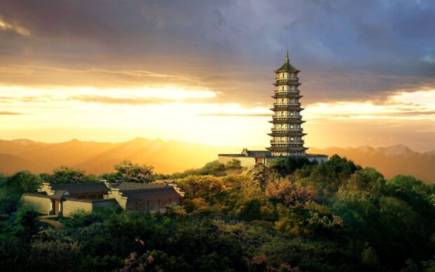 Ancient Asian pagoda surrounded by forest on hill at sunset in Asia