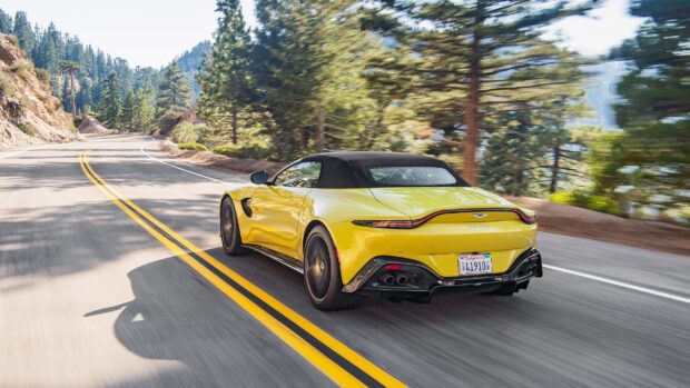 Yellow Aston Martin Vantage driving fast on a mountain road surrounded by trees