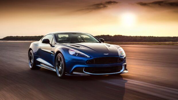 A blue Aston Martin Vantage driving on a track during sunset with trees in the background