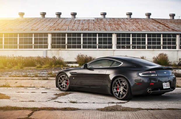 Black Aston Martin Vantage parked near an old industrial building with sunlight glow