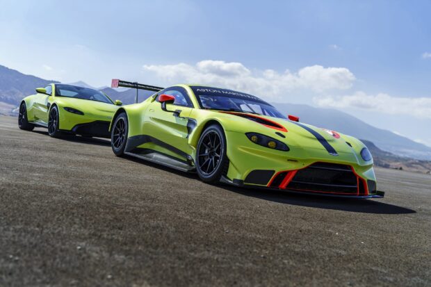 Two Aston Martin Vantage cars parked on a race track with mountains in the background