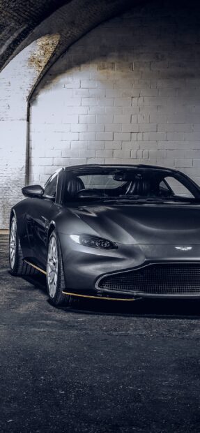 A sleek Aston Martin Vantage parked under an arched brick wall in a dimly lit garage
