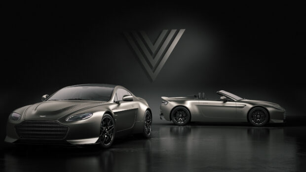 A pair of Aston Martin Vantage models parked in a sleek dark studio with a V logo on the wall