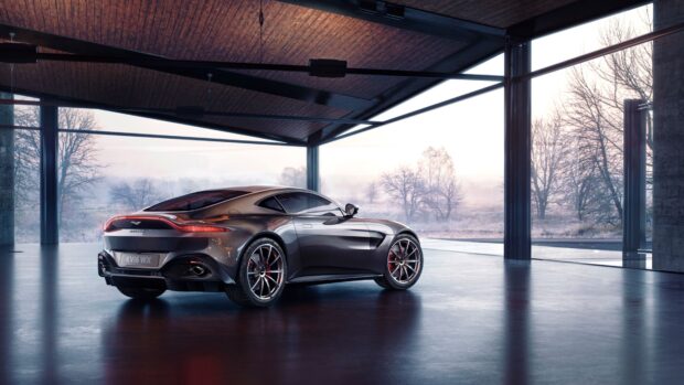 A sleek Aston Martin Vantage parked inside a modern glass garage with a misty landscape outside