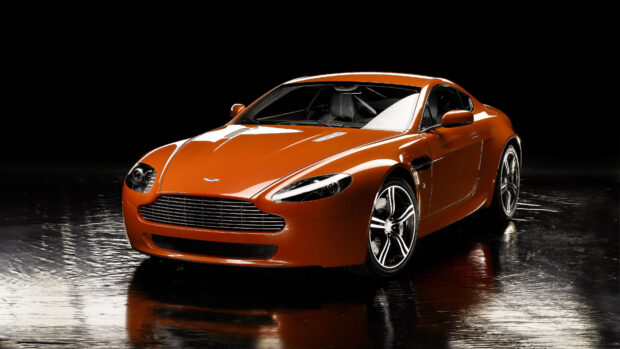 Orange Aston Martin Vantage car parked on a reflective surface in a dark studio setting