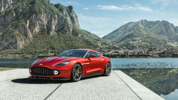 Red Aston Martin Vantage parked near a lake with mountains in the background