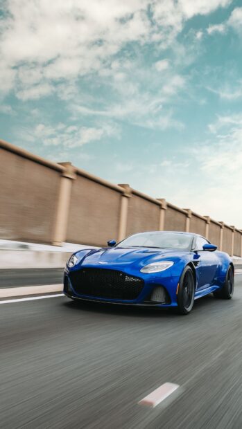 Blue Aston Martin Vantage driving fast on the road under a bright sky