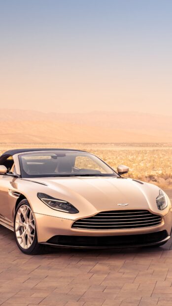 A sleek Aston Martin Vantage parked on a desert road at sunset with mountains in the background