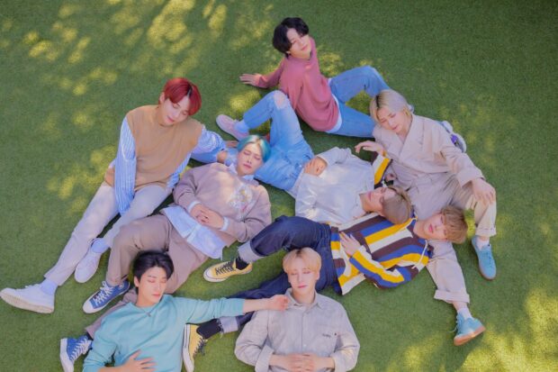 Ateez members relaxing and lying on the grass in casual outfits