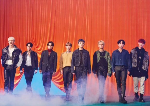 Ateez members standing in front of an orange curtain with smoke on the floor