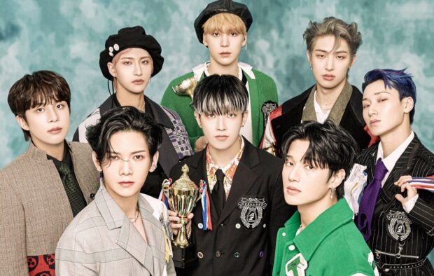 Ateez group posing together in stylish outfits with a trophy in front of a teal background