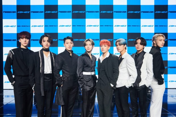 Ateez group standing in front of a blue and white checkered backdrop with stylish outfits