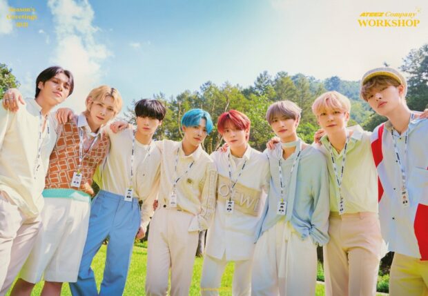 Ateez group standing outdoors in a bright green field on a sunny day