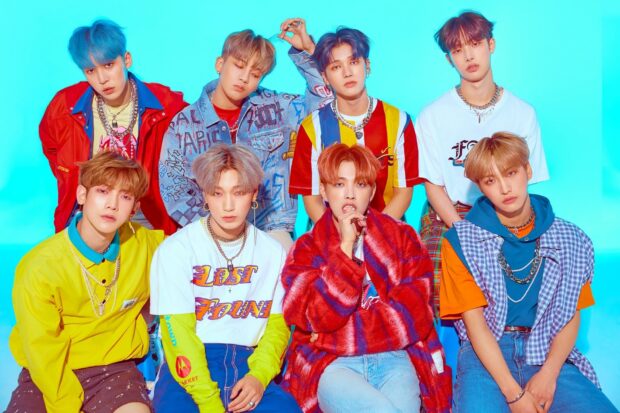 Ateez group members posing in colorful outfits against a bright blue background