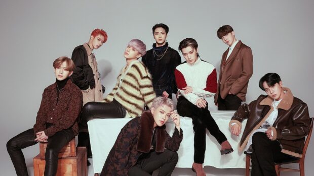 Ateez members posing in fashionable outfits with a minimalist gray background