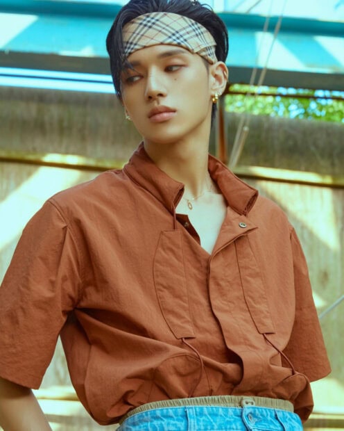 Young male Ateez member wearing a headband and brown shirt looking away outdoors