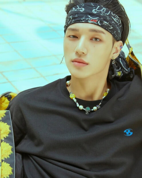 A close up of Ateez member wearing a black bandana and necklace with smiley beads