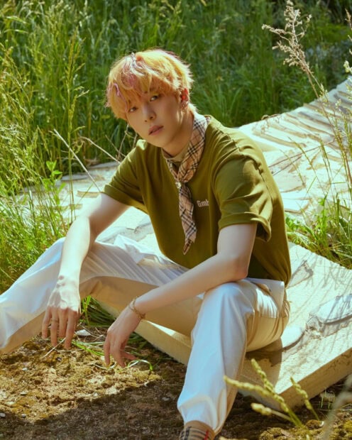 Ateez member sitting outdoors with yellow hair and casual clothing