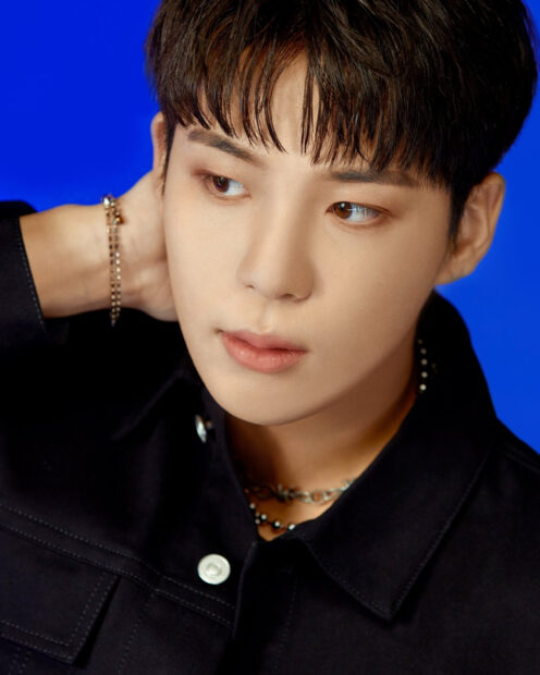 A close up of Ateez member with a blue background and black jacket