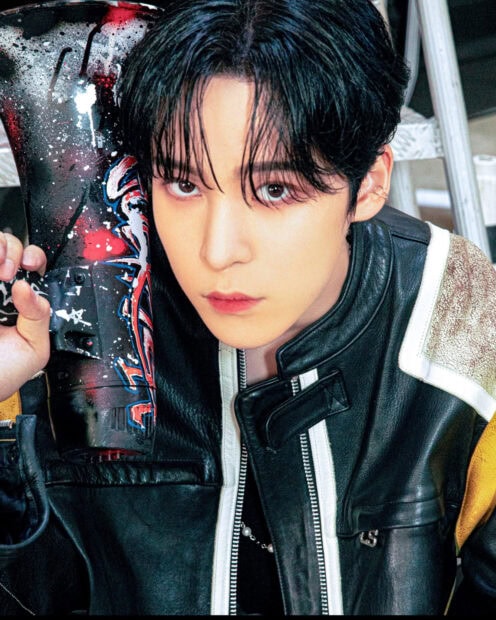 Close up of Ateez member holding a painted skateboard with a serious expression