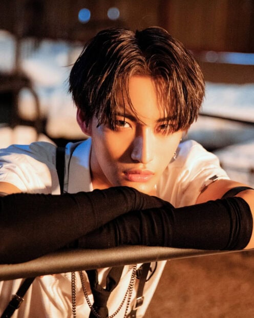 Close up of Ateez member wearing black gloves and white shirt in warm lighting