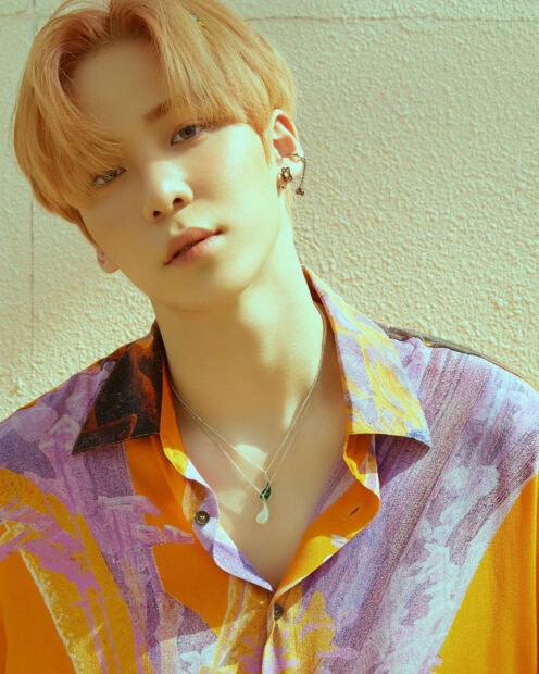 Close up of Ateez member with orange hair wearing a colorful shirt and silver necklaces