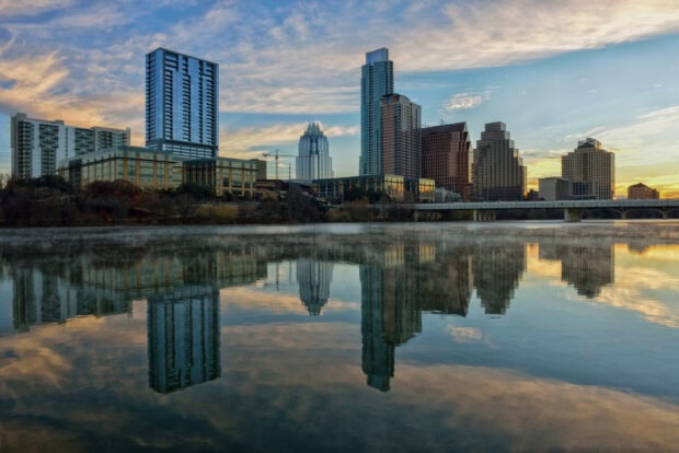 The Austin cityscape reflecting over calm water at sunset with a clear sky