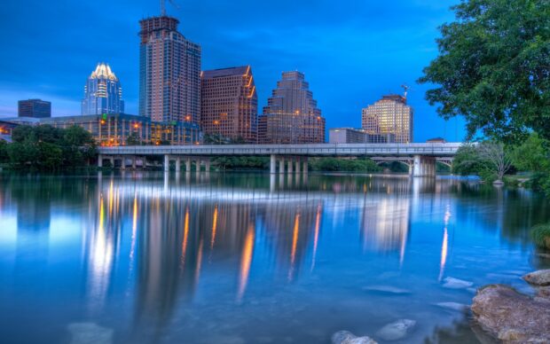 The Austin skyline at dusk with city buildings reflecting on calm river water