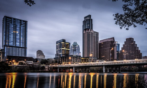 The Austin skyline featuring prominent buildings and a lit bridge over calm water at dusk