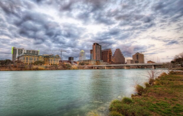View of Austin skyline reflected on river during cloudy weather with cranes and buildings