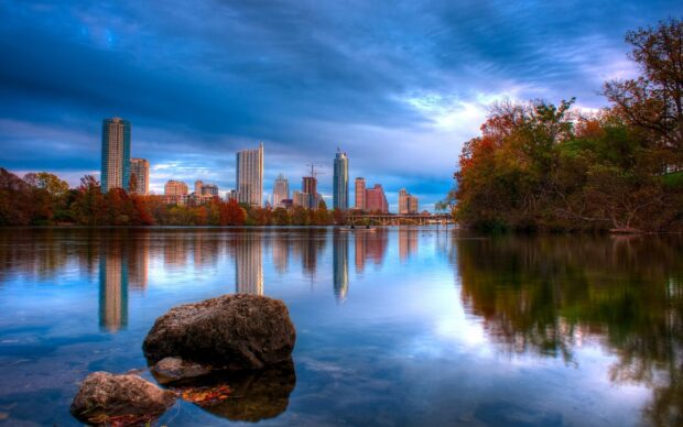 Clear view of Austin skyline reflecting on the calm river with autumn trees